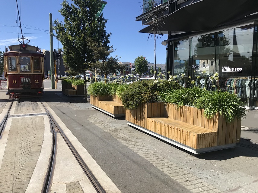 Large planters featuring seating, beside tram tracks
