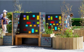 People walk behind a small garden featuring low round planters and stained glass walls