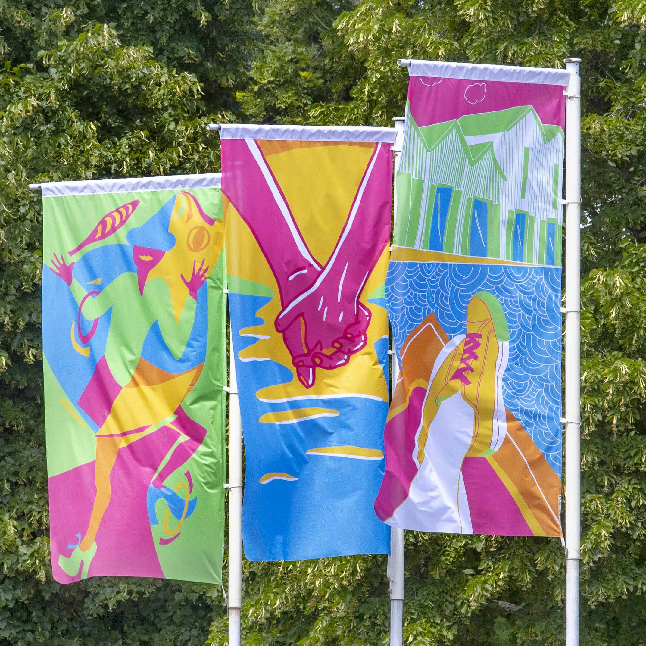 Three colourful street flags displayed beside a tree